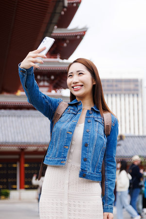 Asian woman taking self photograph with mobile phoneの素材