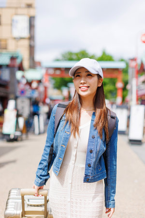Asian woman walking in street with luggageの写真素材