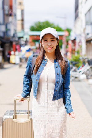 Asian woman walking in street with luggageの写真素材