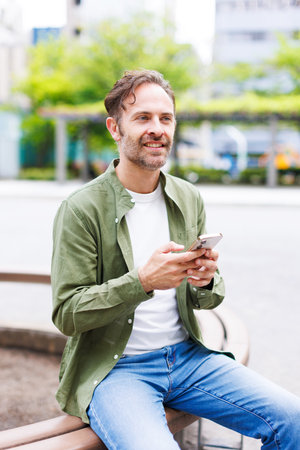Caucasian man with mobile phone sitting outdoorsの写真素材