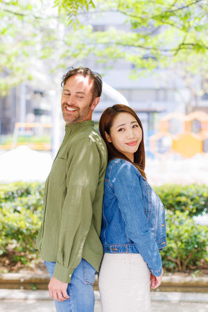 Caucasian man and Asian woman standing back to back and smileの写真素材
