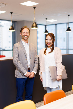 Caucasian businessman and Asian businesswoman in smart casual attire smiling at the camera