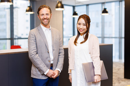 Caucasian businessman and Asian businesswoman in smart casual attire smiling at the cameraの写真素材