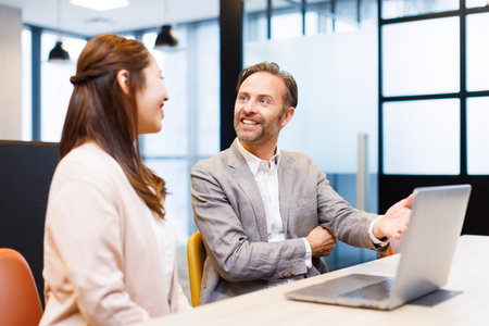 Caucasian businessman and Asian businesswoman in smart casual attire having a discussionの写真素材