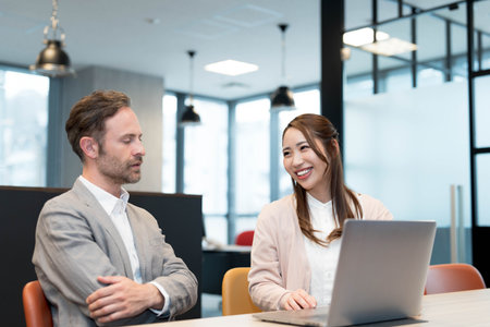 Caucasian businessman and Asian businesswoman in smart casual attire having a discussionの写真素材