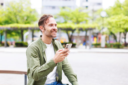 Caucasian man with mobile phone sitting outdoorsの写真素材