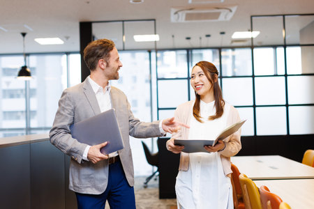 Caucasian businessman and Asian businesswoman in smart casual attire having a discussionの写真素材