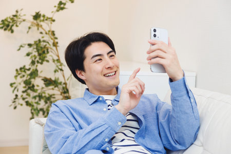 Japanese man using a mobile phone in living roomの写真素材