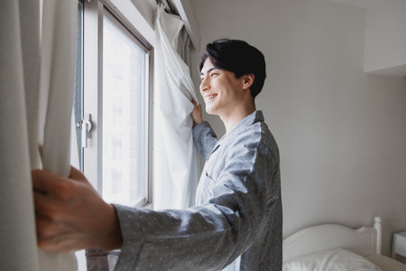 Japanese man in pajamas standing by the windowの写真素材