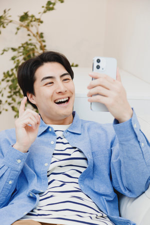 Japanese man using a mobile phone in living roomの写真素材