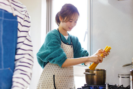 Japanese woman in apron cooking pasta at kitchenの写真素材
