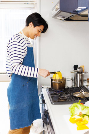 Japanese man in apron cooking pasta at kitchenの写真素材