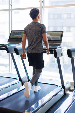 Young Asian man walking on treadmill