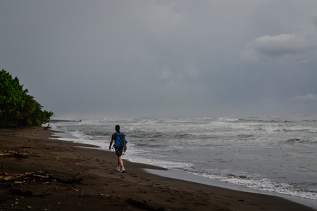 man walking on the beach with dark sandの写真素材