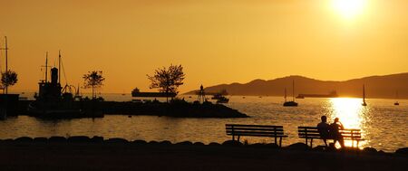 Silhouette of a couple enjoy beautiful sunset view in English Bay, Vancouver Canadaの写真素材