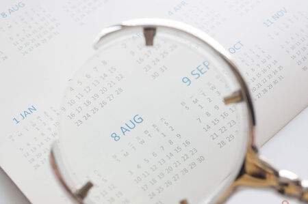 Hand holding magnifying glass to checking calendar of Augustの写真素材