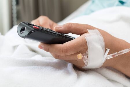 Female Patient watching TV and remote control in hand In Hospital Bedの写真素材