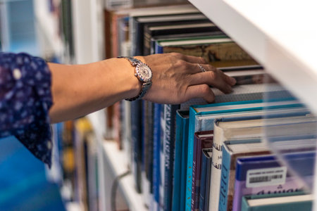 Close up shot of a woman's hand reaching out for the book in the bookshelfの写真素材