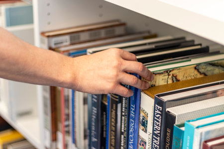 Close up shot of a man's hand reaching out for the book in the bookshelf