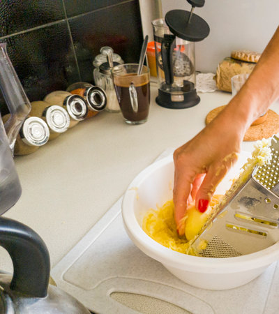 Woman grinding potatoes on the grater in the kitchen.の写真素材