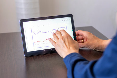 Close up shot of the woman with beautiful hands , using tablet, studying mortgage sales report