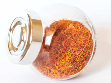 Close up shot on the white background of the dried saffron leaves spice in a small glass jar containerの写真素材
