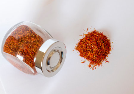 Close up shot on the white background of the dried saffron leaves spice in a small glass jar container.の写真素材