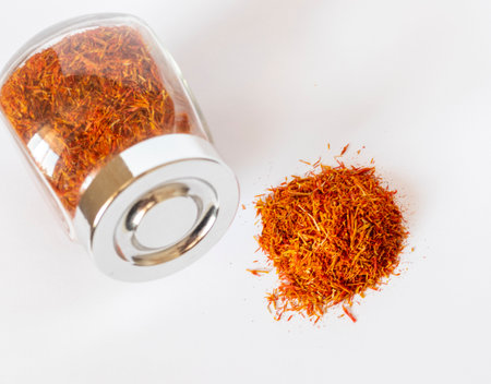 Close up shot on the white background of the dried saffron leaves spice in a small glass jar container.の写真素材