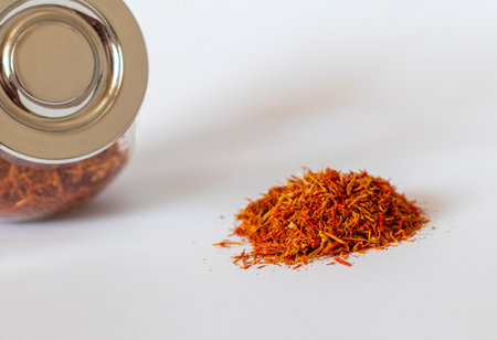 Close up shot on the white background of the dried saffron leaves spice in a small glass jar container.の写真素材