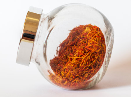Close up shot on the white background of the dried saffron leaves spice in a small glass jar containerの写真素材