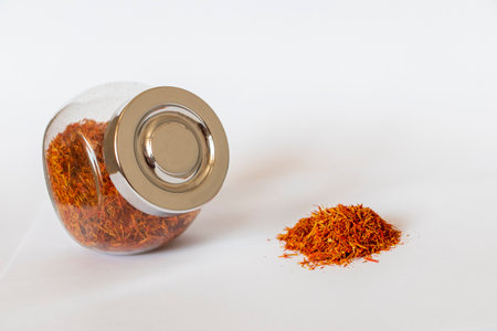 Close up shot on the white background of the dried saffron leaves spice in a small glass jar container.の写真素材