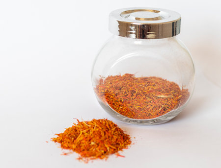Close up shot on the white background of the dried saffron leaves spice in a small glass jar containerの写真素材