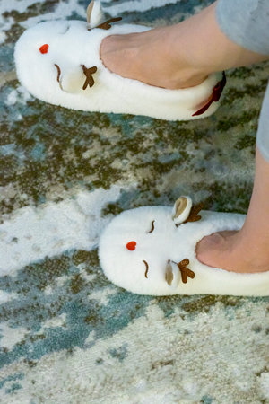 Woman wearing funny, deer shaped, soft christmas shoes. Playfully moves them in front of christmas tree.の写真素材