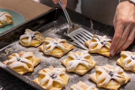 A woman pick the fruit puff pastries with spatula from baking tray and places them on ceramic plateの写真素材