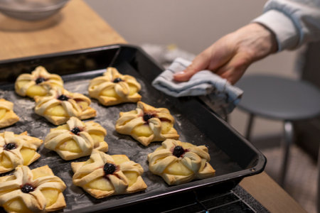 A woman places baking tray with with puff pastry with pineapple wedges wrapped and cherry on top from the oven to the kitchen counter topの写真素材