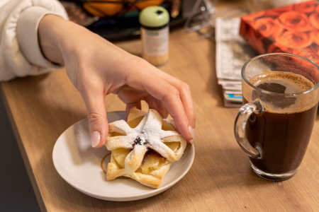 A woman picks freshly baked fruit puff pastry on the ceramic plate next to hot cup of coffeeの写真素材