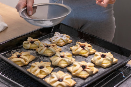 A woman dusts a pineapple wedge and cherry wrapped in a puff pastry with powdered sugar