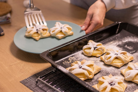A woman pick the fruit puff pastries with spatula from baking tray and places them on ceramic plateの写真素材