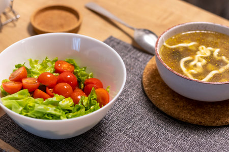 Bowl with cherry tomatoes and lettuce leaves, bowl with soup next to itの写真素材
