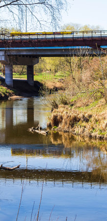 Yellow bus crossing the bridge, casting reflection in the waterの写真素材