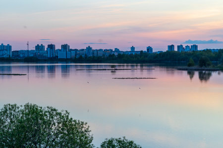 Sun is setting by the lake with city buildings on the backgroundの写真素材