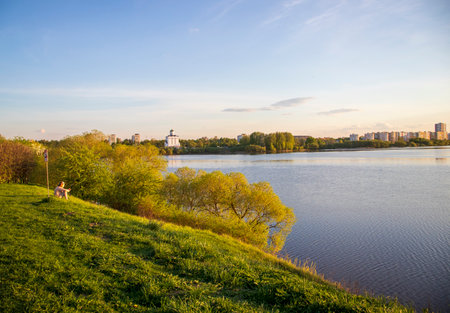 Minsk, Belarus - 05.04.2025 - Sun is setting by the lake with city buildings on the backgroundの写真素材
