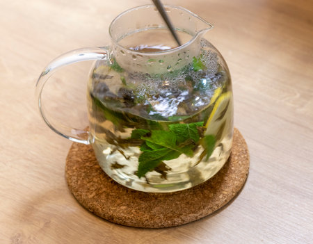 Stylish transparent tea pot with just brewed green tea leaves, mint leaves and lemon slices in itの写真素材
