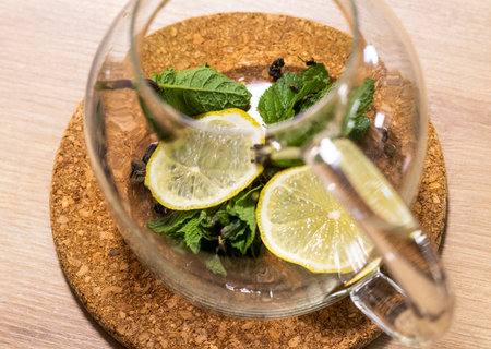 Stylish transparent tea pot with dried tea leaves, mint leaves and lemon slices in itの写真素材