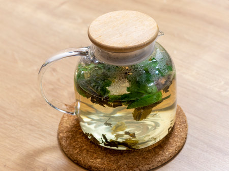 Stylish transparent tea pot with just brewed green tea leaves, mint leaves and lemon slices in itの写真素材
