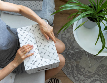 Woman sitting in the couch in cozy room, assembling carton boxの写真素材