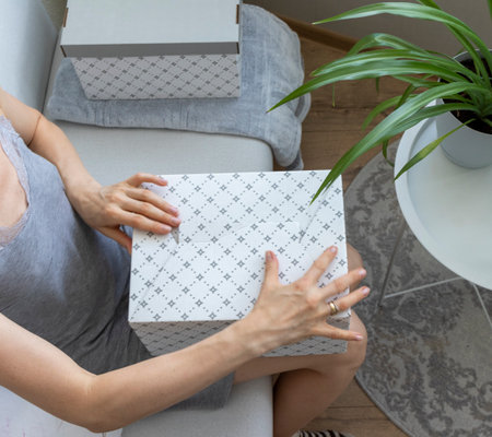 Woman sitting in the couch in cozy room, assembling carton box.