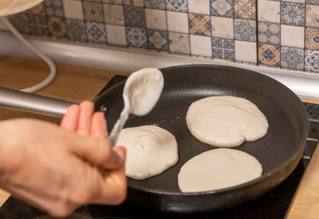 Woman pours pancake dough in to the frying pan