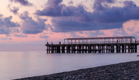 Concept shot of the men fishing on the abandoned pier, bridge made of metal bars during dramatic sunsetの写真素材