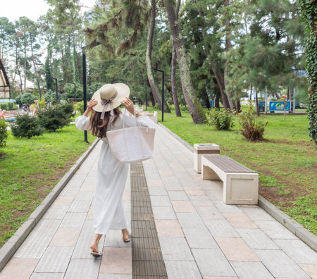 Attractive woman wearing creamy, off white outfit, straw hat in the park for a walkの写真素材